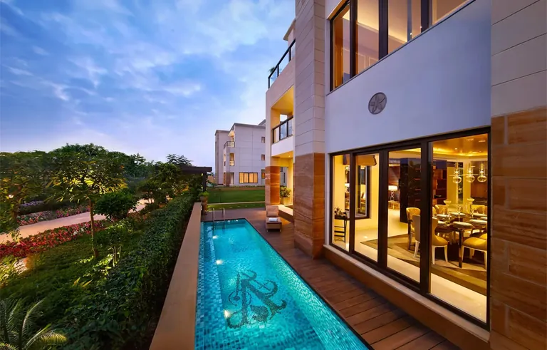 BPTP Astaire Gardens villa with a private lap pool and glass-fronted living room at dusk