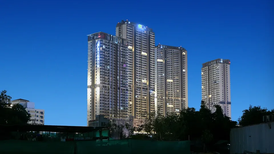 M3M Heights completed towers lit up against the evening sky, seen from the road