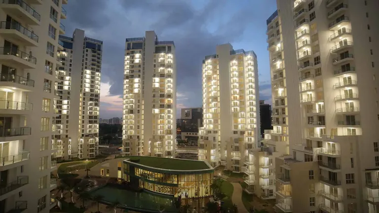 M3M Merlin towers lit up at dusk around the clubhouse with its green roof, artist's impression